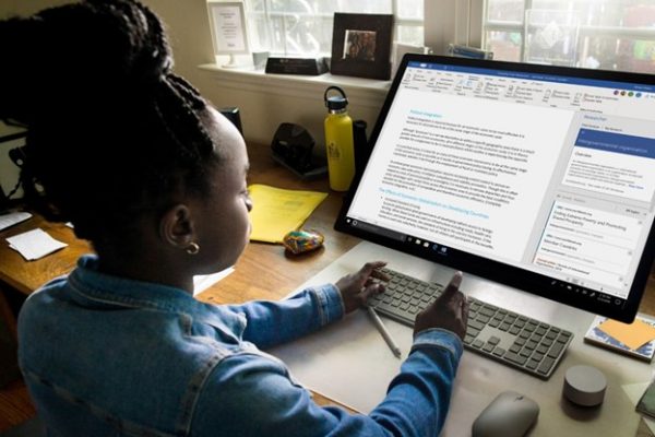 TTT_Improve-Your-Workplace-Productivity-with-Microsoft-Word-11-Tips-to-Make-the-Most-of-this-Program-Featured-Image.jpg Young person using a wireless keyboard to work on a document in Microsoft Word on a large desktop monitor