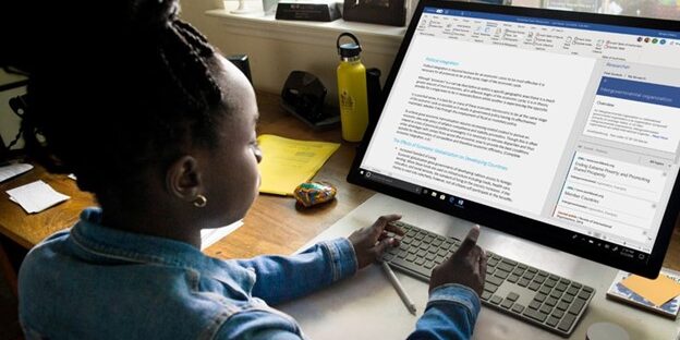 TTT_Improve-Your-Workplace-Productivity-with-Microsoft-Word-11-Tips-to-Make-the-Most-of-this-Program-Featured-Image.jpg Young person using a wireless keyboard to work on a document in Microsoft Word on a large desktop monitor