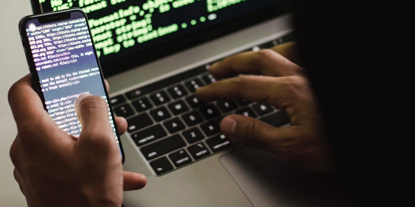 Mobile-Malware-Has-Increased-500-What-Should-You-Do-scaled.jpg Free Unrecognizable hacker with smartphone typing on laptop at desk Stock Photo