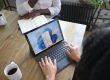 Overhead view of two people at a table working with a Microsoft laptop and notebook